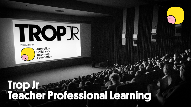 A crowded cinema hall is filled with attendees seated in rows, all facing a large screen displaying the logo for "TROP JR" and the phrase "Teacher Professional Learning," alongside the logo of the Australian Children's Television Foundation. The environment is dimly lit, typical for a movie screening.