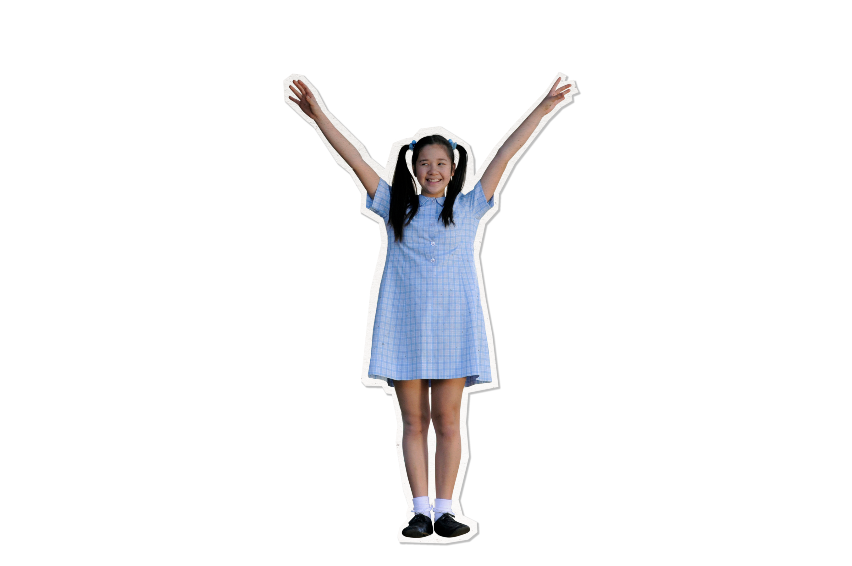 A young girl in a light blue plaid dress raises her arms enthusiastically, wearing black shoes and white socks. She has dark hair styled in pigtails and is smiling widely, exuding happiness and energy.