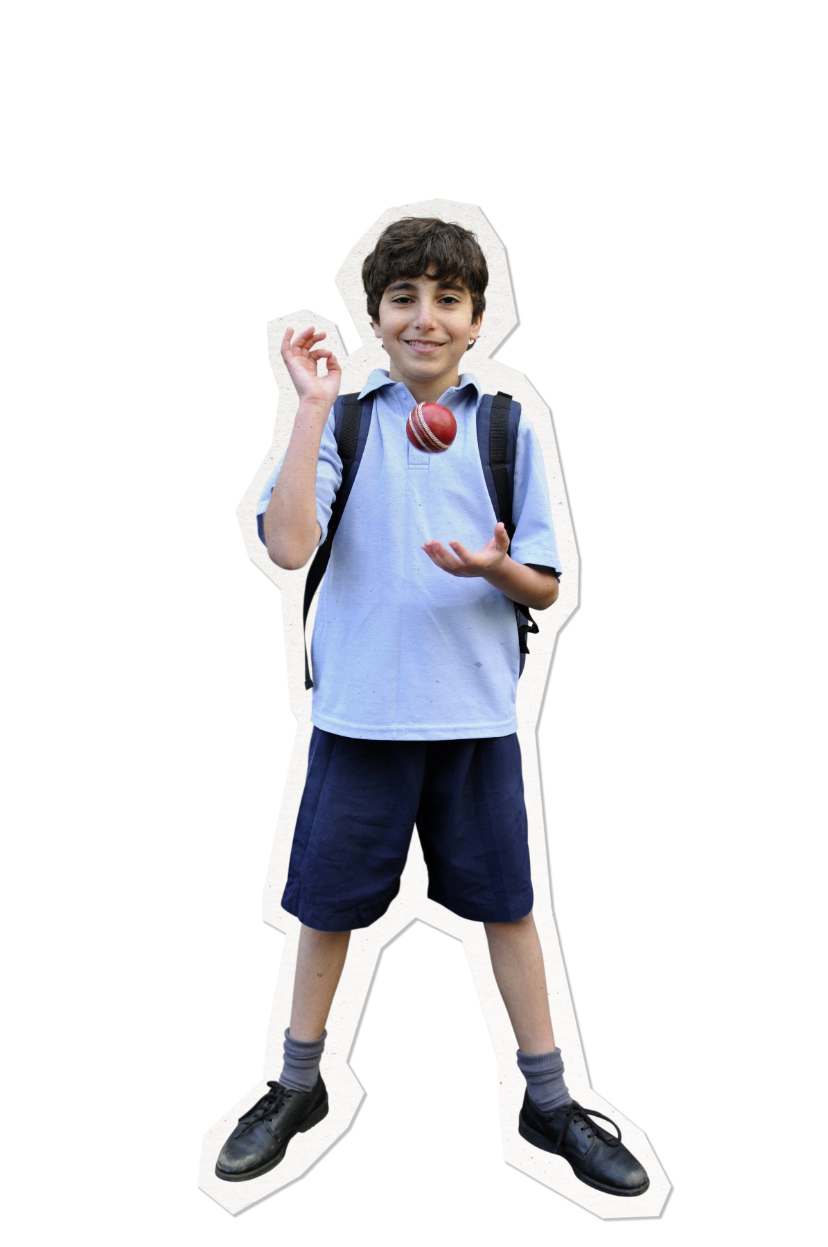 A young boy with curly hair stands confidently while holding a cricket ball in one hand and gesturing with the other. He wears a light blue polo shirt, navy shorts, and black shoes, with a backpack slung over one shoulder.