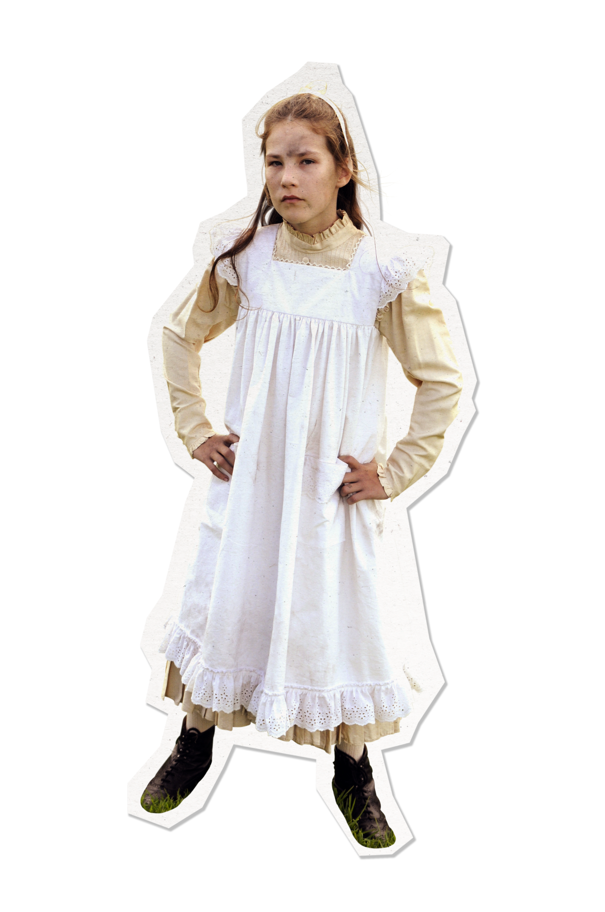 A girl stands confidently with her hands on her hips, dressed in a vintage white dress with lace trim over a long-sleeved beige shirt. Her long brown hair is partly pulled back, and she wears black boots. The background is plain, emphasizing her posture and attire.