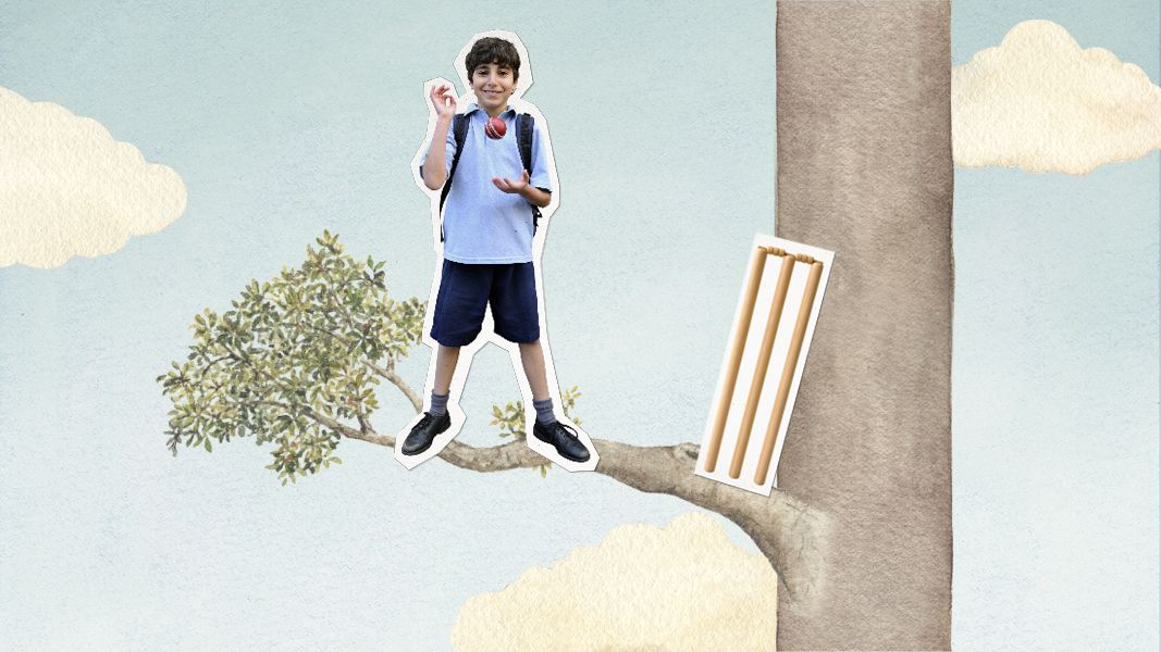 A young boy in a blue shirt and shorts stands confidently on a tree branch, holding a red toy while looking joyful. Nearby, a piece of white paper is attached to the tree trunk, displaying several brown sticks. The background features a light blue sky with fluffy clouds.
