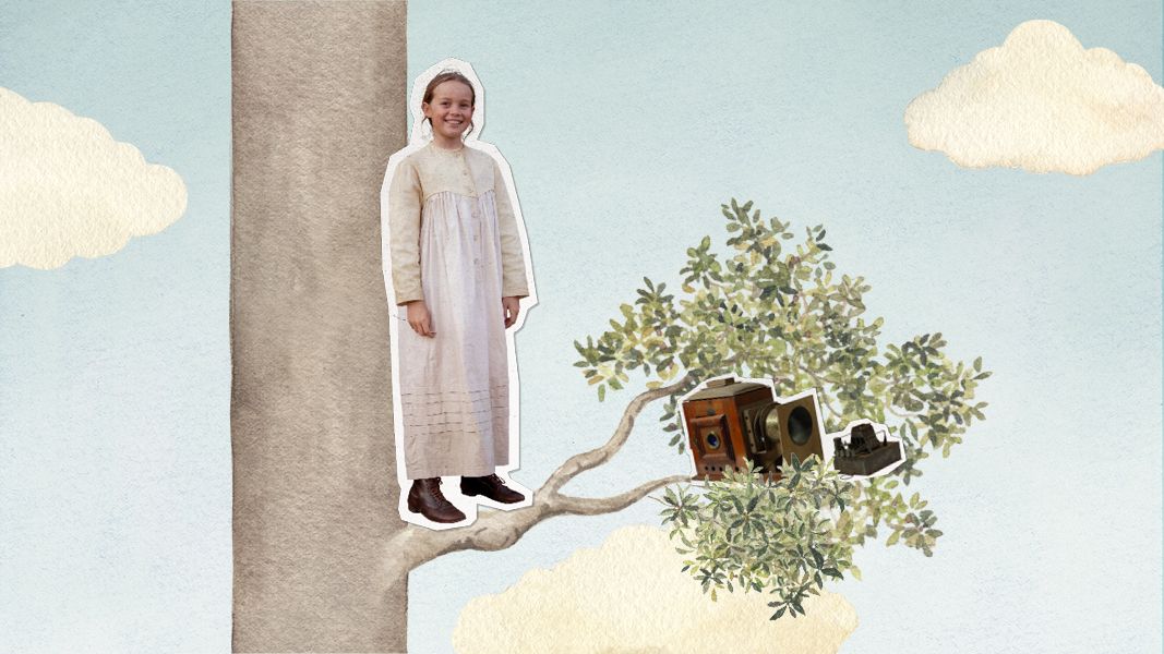 A young girl stands on a branch of a tree, wearing a long, light-colored dress and brown boots. Next to her, an old-fashioned camera and other vintage items are nestled among the leaves, all set against a pastel blue sky with fluffy white clouds.